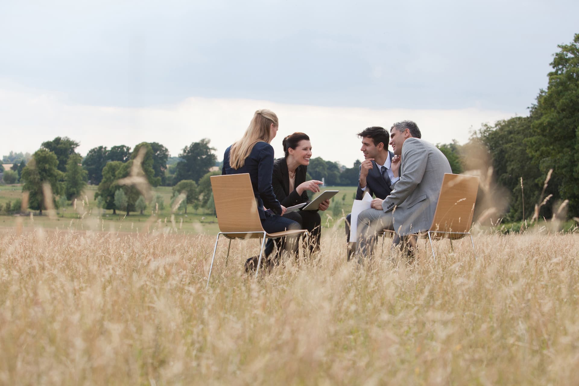 Vier professionals in gesprek op stoelen in een open veld